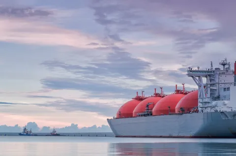 Liquefied natural gas (LNG) carrier ship with large red storage tanks docked at port during sunrise, representing global energy trade and natural gas exports.